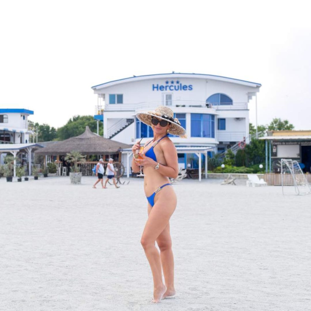 Turist care se relaxează cu un cocktail pe plaja jupiter, cu Hotelul Hercules în fundal