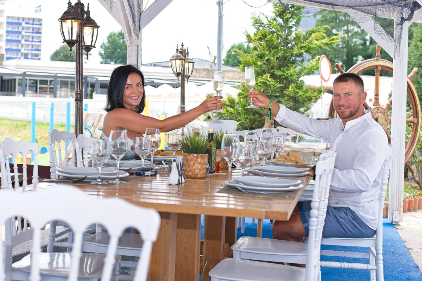 Două persoane ciocnind paharele la masa de pe terasa restaurantului Hotel Hercules