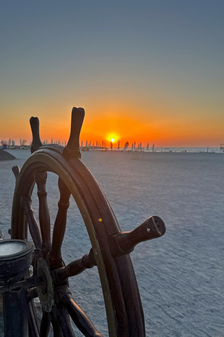 Cârmă de corabie decorativă din lemn pe nisipul plajei Hotel Hercules cu mare în fundal