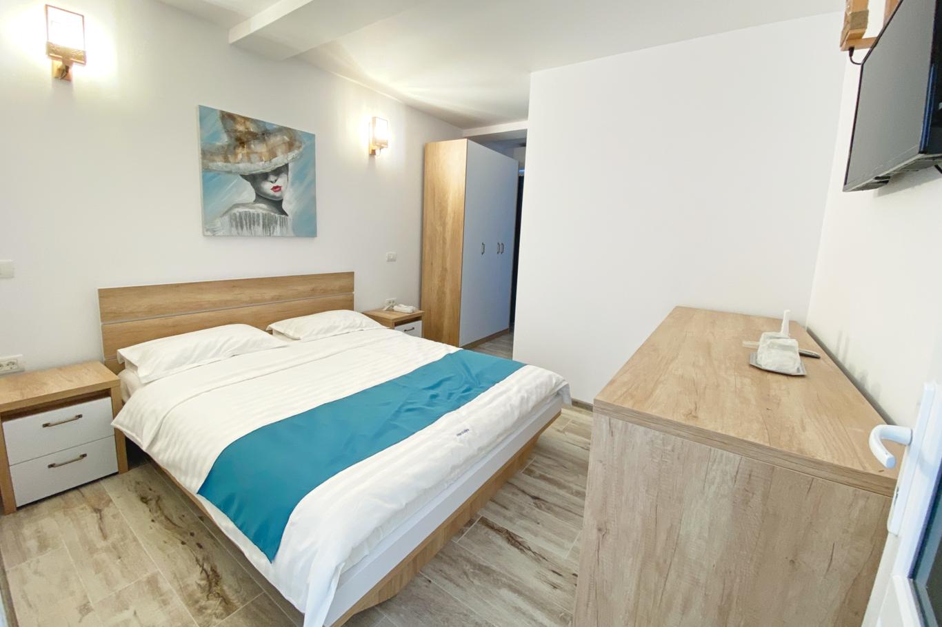 Cameră luminoasă cu pat matrimonial, lenjerie albă și turcoaz și parchet din lemn