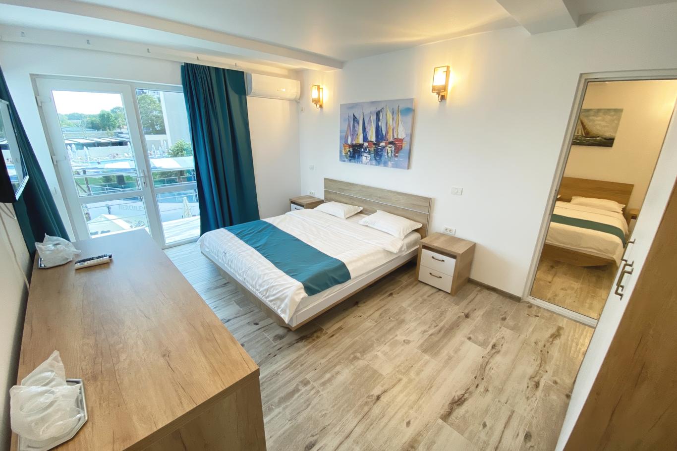 Cameră cu pat matrimonial, decor în tonuri alb-turcoaz și parchet din lemn deschis