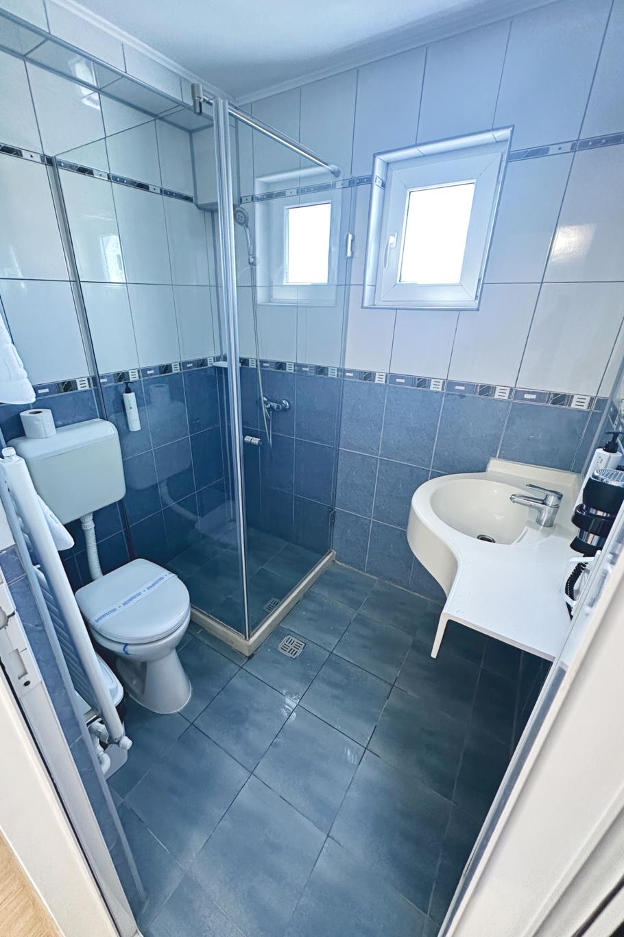 Baie modernă cu gresie închisă, cadă, toaletă și chiuvetă, iluminare integrată