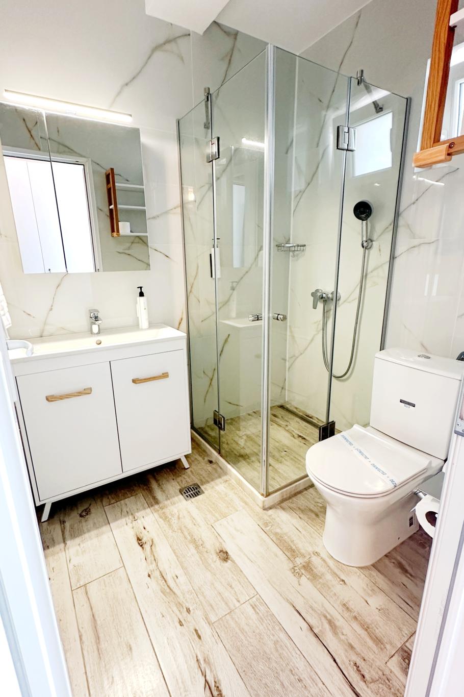 Baie modernă renovată cu cabină de duș, gresie deschisă și dotări sanitare complete