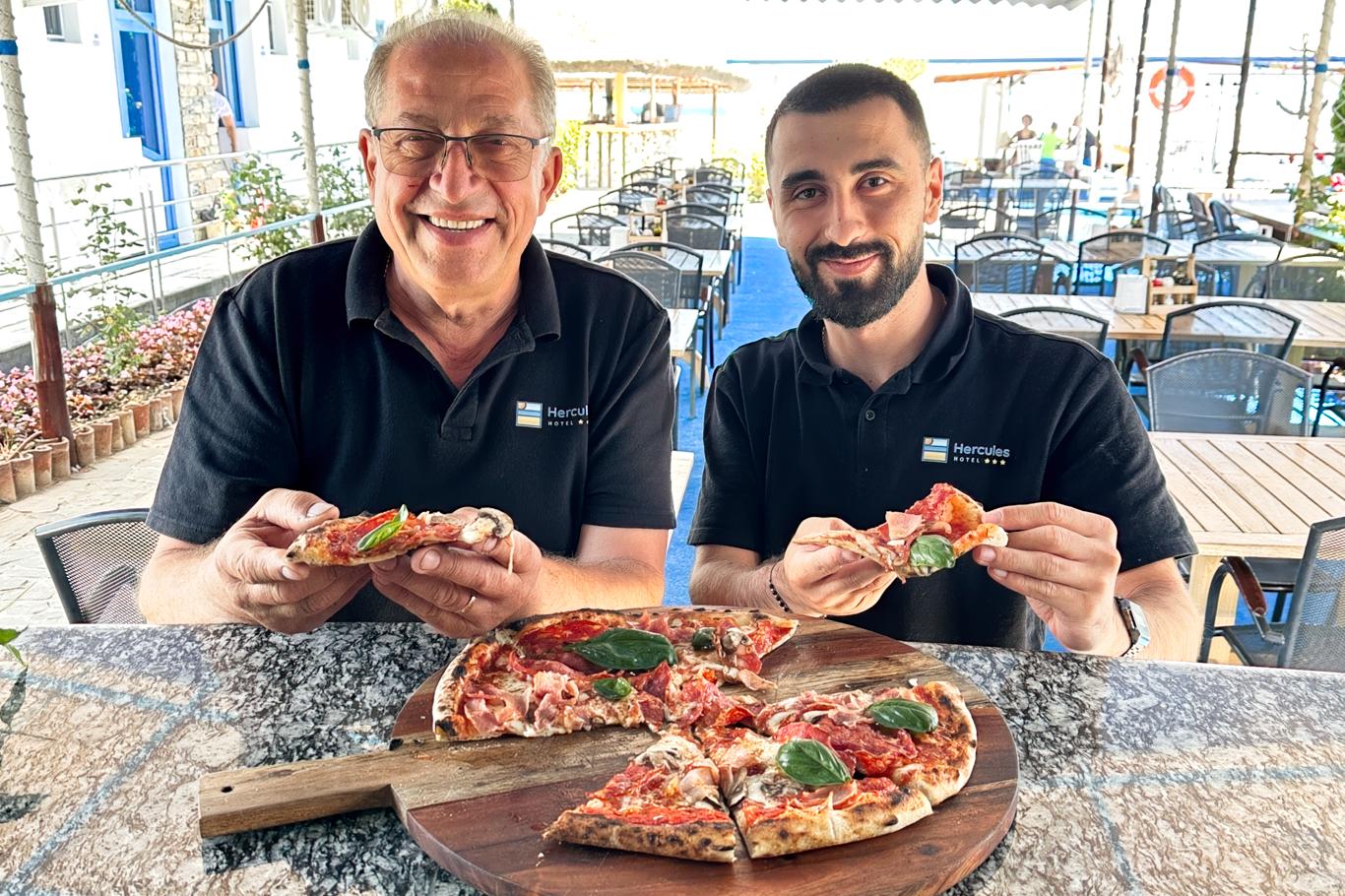 Doi bărbați zâmbitori prezentând o pizza pregătită în restaurantul Hotel Hercules