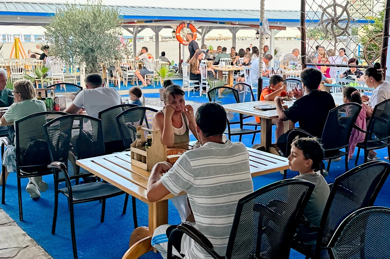 Terasă animată cu oaspeți la micul dejun, cu mobilier colorat și atmosferă prietenoasă